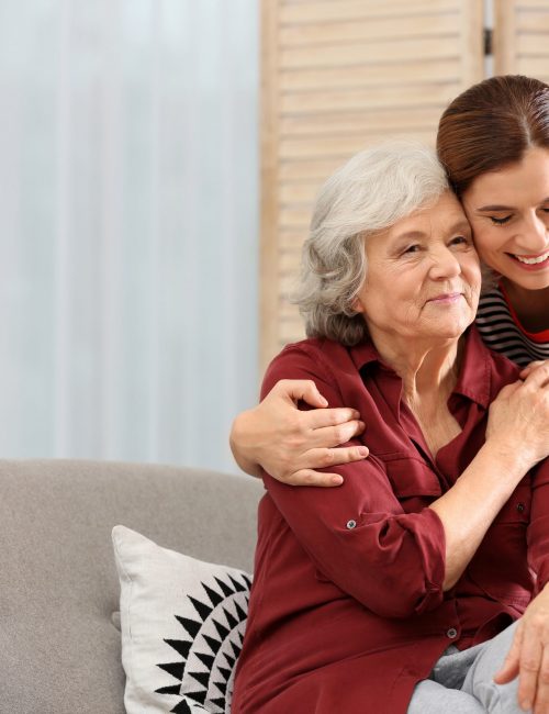 Elderly woman with female caregiver in living room. Space for text
